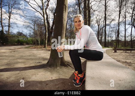 Weibliche Läufer eine Pause vom laufen im Wald. Schöne junge Sportlerin sitzen mit einer Flasche Wasser. Stockfoto