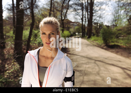 Porträt der hübschen jungen Frau im Sport Kleidung tragen Kopfhörer während des Fitness-Routine im Wald. Junge weibliche Läufer Stockfoto