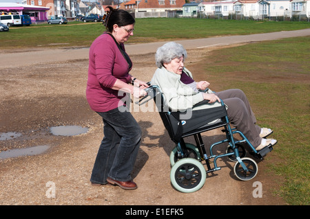 Alte Dame im Rollstuhl mit Rädern über unebenem Boden von ihrem Betreuer oder Helfer. Stockfoto