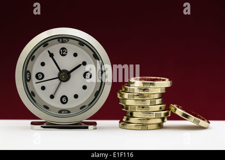 Uhr mit einem Stack von Goldmünzen, die zur Veranschaulichung der Konzepte von Zeit ist Geld oder finanzielle Termindruck. Stockfoto