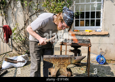Schmied benutzt einen Hammer und Amboss, eine Eisenstange zu gestalten Stockfoto