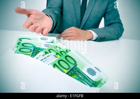 ein Mann in einem Anzug sitzt in einem Schreibtisch nehmen einen Umschlag voller Euro-Scheine Stockfoto