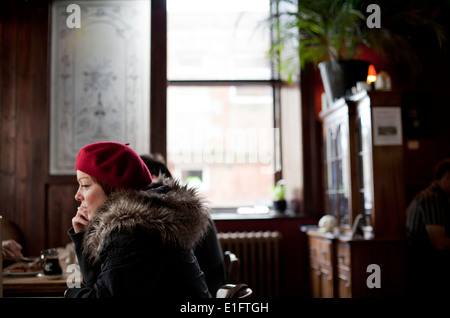 Frau im roten Hut sitzt allein im Café Rose Blatt in Edinburgh, Schottland. Stockfoto