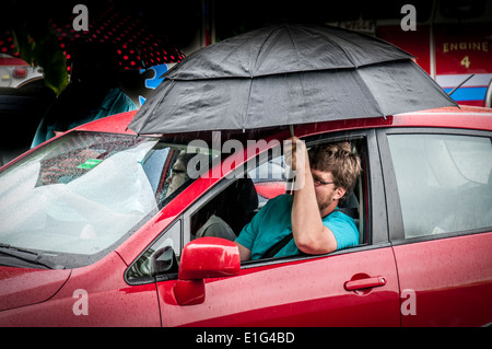 Trocken zu halten, dieser Mann, während gerade eine Parade in einem Regen Sturm rollten seine Fenster, einen Regenschirm in Aufmachungen besser hören die Musik. Stockfoto