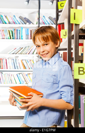 Schuljunge steht und hält Bücher in der Bibliothek Stockfoto