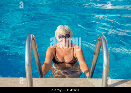 Alte Frau glücklich lächelnd am Rand des Pools, die Handläufe festhalten. Stockfoto