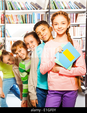 Glückliche Kinder stehen hintereinander in Bibliothek Stockfoto