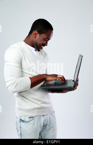 Afrikanischer Mann mit Laptop beim Aufstehen auf grauem Hintergrund Stockfoto