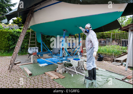 Ein Mann, gekleidet in Schutzkleidung, den Rumpf einer Yacht malen Stockfoto