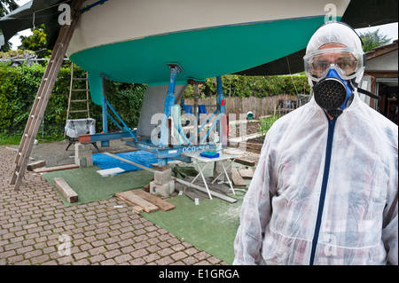 Ein Mann, gekleidet in Schutzkleidung, bereit, den Rumpf einer Yacht malen Stockfoto