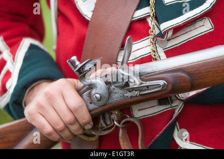 Ein Soldat gekleidet in traditionellen 17. Jahrhundert englische Armee Rotrock einheitliche laden eine Steinschlossmuskete. Stockfoto