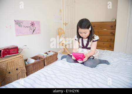 Junges Mädchen sitzt auf Bett Computerspiel Stockfoto
