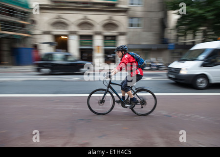Mann trägt eine rote Jacke, Helm und tragen einen Rucksack Fahrten seinem Mountainbike entlang einer Londoner Straße. Stockfoto