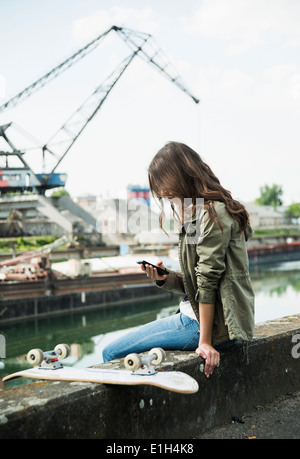 Junge Frau sitzt an Wand mit Handy Stockfoto