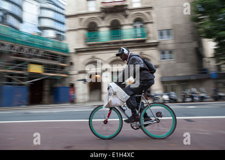 Mann mit Kopfhörern über seine Baseball-Cap, reitet ein Fahrrad mit leuchtend blauen Rädern entlang einer Londoner Straße. Stockfoto