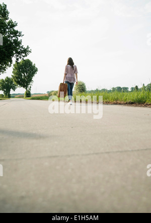 Junge Frau zu Fuß auf Landstraße mit Koffer Stockfoto