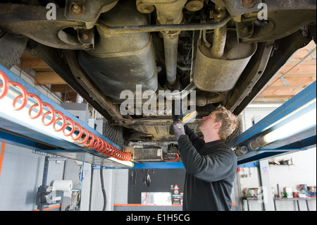 Ein Mechaniker prüft die technischen Zustand unter einer angehobenen Auto auf einer Brücke in einer Garage. Stockfoto