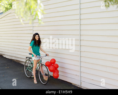 Porträt der jungen Frau mit dem Fahrrad und einem Haufen Luftballons Stockfoto