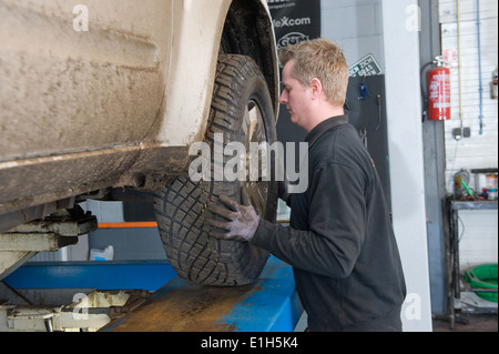 Ein Mechaniker wandelt sich das Rad von einem angehobenen Auto auf einer Brücke in einer Garage. Stockfoto