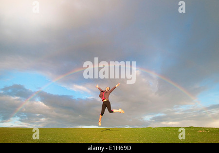 Junge weibliche Wanderer springen Luft unter Regenbogen Stockfoto