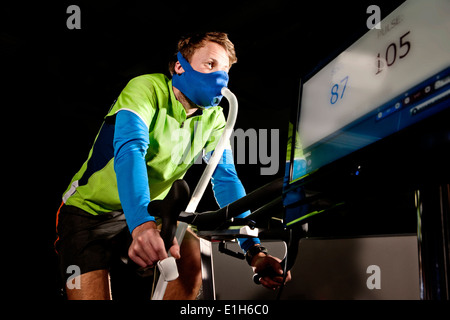 Junger Mann in Gesichtsmaske auf Fitness-Studio trainieren Zyklus in Höhe Mitte Stockfoto