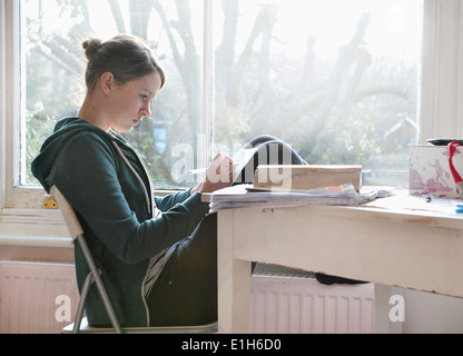 16 Jahre alten Mädchen studieren und Schreiben von Notizen neben Fenster Stockfoto