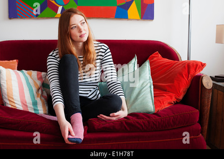 Junge Frau sitzend auf Sofa mit Füßen Stockfoto