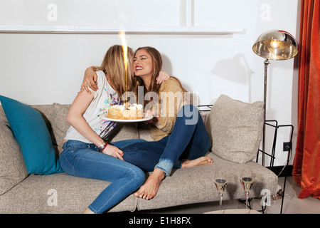 Junge Frauen mit Kuchen umarmt auf couch Stockfoto