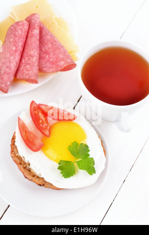 Frühstück - Sandwich mit Spiegelei, Tomatenscheiben und Tee auf Holztisch Stockfoto