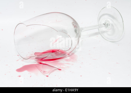 Zerbrochene Weinglas mit scharfen Scherben und verschüttete Schuss Rotwein auf weißem Hintergrund Stockfoto