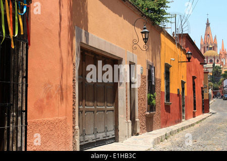 Häuser, die entlang einer gepflasterten Straße mit La Parroquia Kirche in der Ferne in San Miguel de Allende, Guanajuato, Mexiko Stockfoto