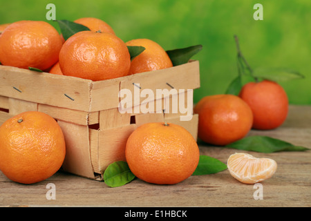 Mandarinen mit Blättern in einer Holzkiste auf einem Tisch mit grünem Hintergrund Stockfoto