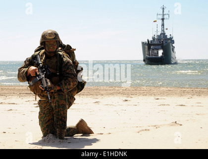 US Marine Corps Sgt. Christopher Judy hält position an einem Strand mit dem polnischen Schiff ORP Krakau im Hintergrund während einer Stockfoto