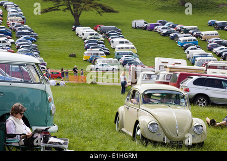 Frau saß neben dem Volkswagen-Wohnmobil mit einem VW-Käfer fahren bergauf auf einem Feld-Parkplatz Stockfoto