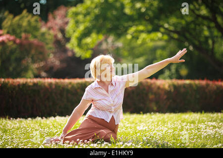 Meditation. Anmutig alte Frau im Park ihre Hand dehnen Stockfoto