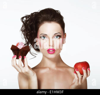 Dilemma. Ernährung. Unentschlossen Frau mit Apfel und Cupcake Stockfoto