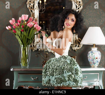 Schöne glamouröse Frau in Retro-Interieur mit Vase mit Blumen. Reflexion Stockfoto