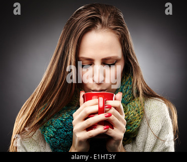 Nahaufnahme einer Frau mit Grippe in ein Tuch gewickelt und trinken heißen Tee über grauen Hintergrund Stockfoto