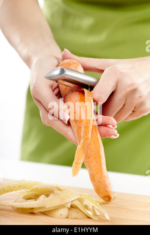 Hände einer jungen Frau schälen von Karotten und Kartoffeln auf einem Holzbrett Stockfoto