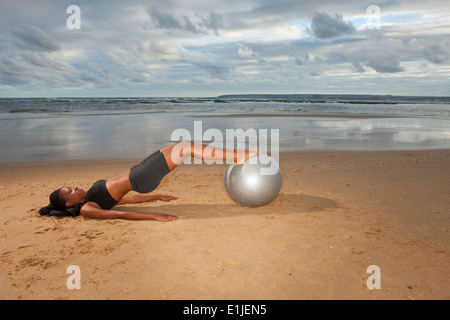 Junge Frau praktizieren Yoga mit Gymnastikball am Strand Stockfoto