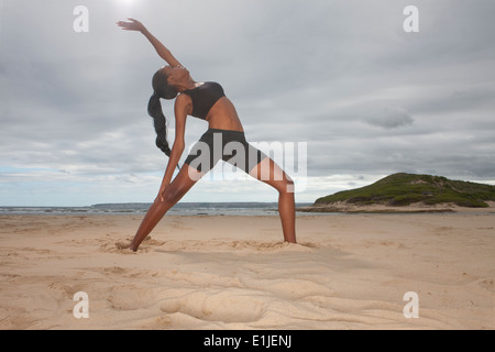Junge Frau praktizieren Yoga Stellung am Strand Stockfoto