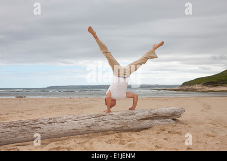 Junger Mann macht Handstand auf Baumstamm am Strand Stockfoto