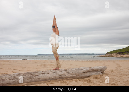 Schwanger Mitte Erwachsene Frau praktizieren Yoga auf Baumstamm am Strand Stockfoto