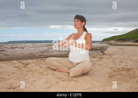 Schwanger Mitte Erwachsene Frau praktizieren Yoga am Strand Stockfoto