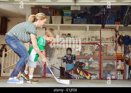 Mutter spielt Hockey in Garage mit zwei Söhne Stockfoto