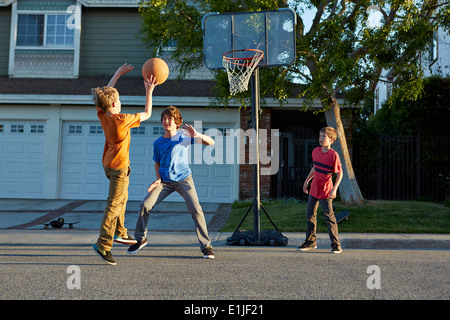 Jungen spielen Basketball vor Haus Stockfoto