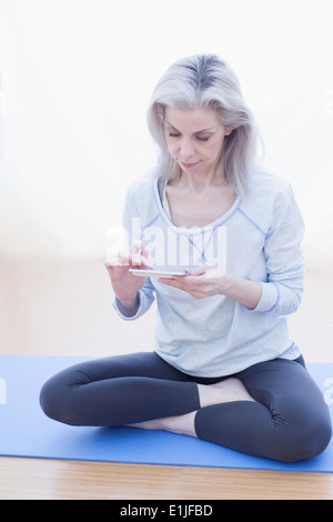 Reife Frau in Lotus-Pose, mit Mobiltelefon Stockfoto