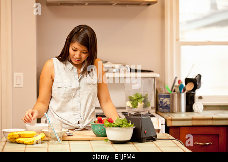 Junge Frau, die die grünen Smoothies in Küche Stockfoto