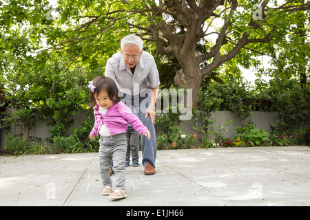 Großvater, Himmel und Hölle mit Kleinkind Enkelin spielen Stockfoto