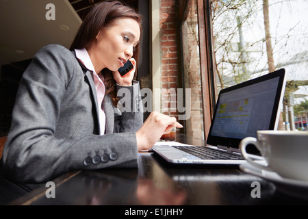 Junge weibliche Unternehmerin mit Laptop und Smartphone im café Stockfoto